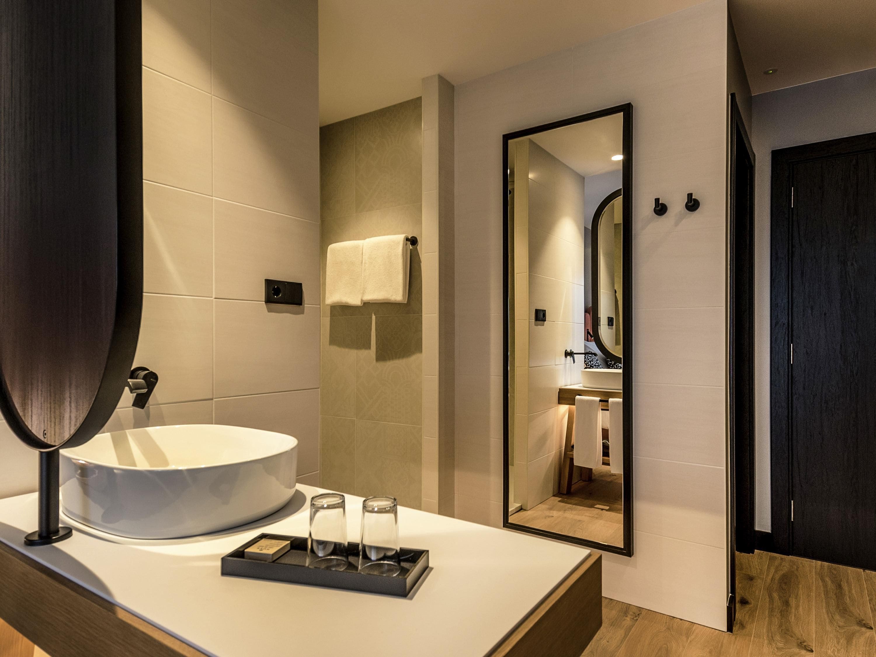 A modern bathroom with a large mirror, a round sink, and a tray with two glasses.