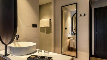 A modern bathroom with a large mirror, a round sink, and a tray with two glasses.