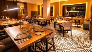 Un restaurant modern amb diverses taules de dinar, cadascuna preparada amb plats, gots i coberts. El sòl té un disseny de rajoles geomètric, i l'espai està il·luminat amb una llum càlida.