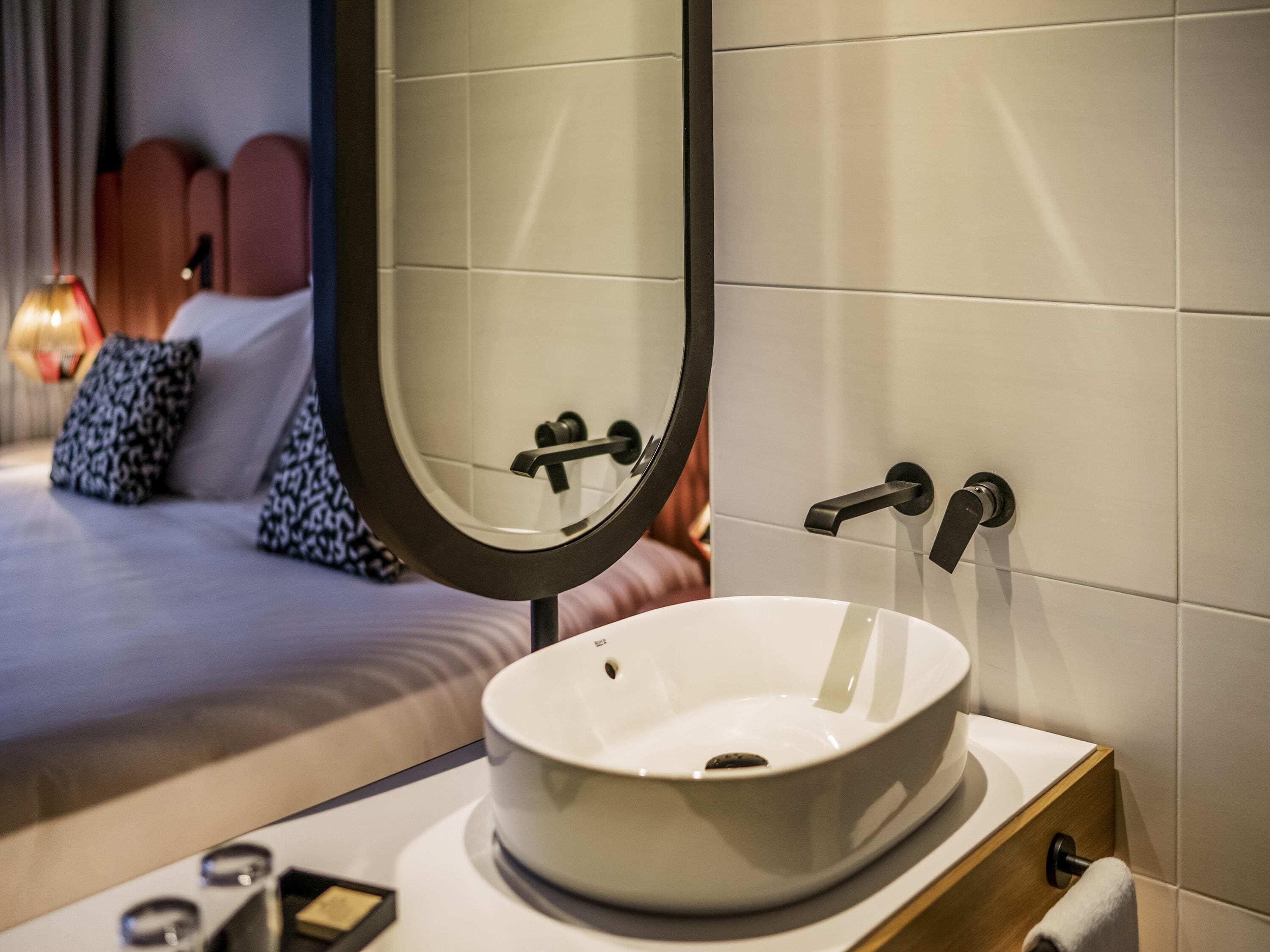 A modern bathroom with a round sink, a mirror, and a towel rack.