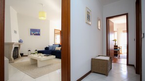 Een woonkamer met een bank, salontafel en een open haard. Een gang leidt naar een andere kamer met een eethoek.