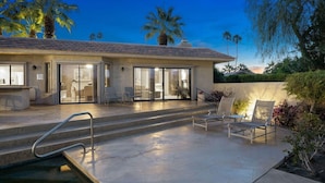 Ein modernes Haus mit Terrasse, Sitzgelegenheiten im Freien und einem Pool.