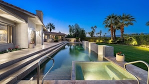 Ein Pool mit Stufen, die zu einem Haus führen, umgeben von Palmen und einem gepflegten Rasen.