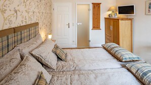 A bedroom with a bed, pillows, a bedside table with a lamp, a wardrobe, and a television on the wall.