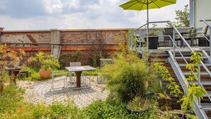 A rooftop garden with a table and chairs, a yellow umbrella, and a staircase.
