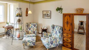 A living room with two patterned armchairs, a wooden cabinet, a plant, and a vintage radio.