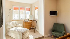 Un dormitorio con cama, escritorio, silla, televisión y ventana con persianas.