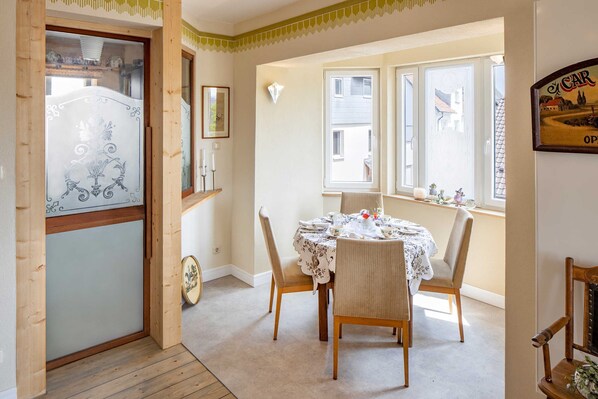 A dining area with a round table, two chairs, a window with a view of buildings, and a door with a frosted glass panel.