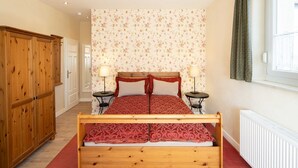 Un dormitorio con una cama de madera, dos mesitas de noche con lámparas, un radiador y un armario.