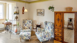 A living room with two patterned armchairs, a wooden cabinet, a plant, and a vintage radio.