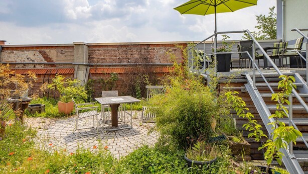 A rooftop garden with a table and chairs, a yellow umbrella, and a staircase.