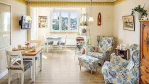 A cozy living room with a dining area, wooden floors, and a view through the window.
