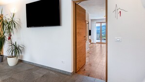Een modern interieur met een flatscreen tv aan de muur, een houten deur naar een andere kamer en een potplant.