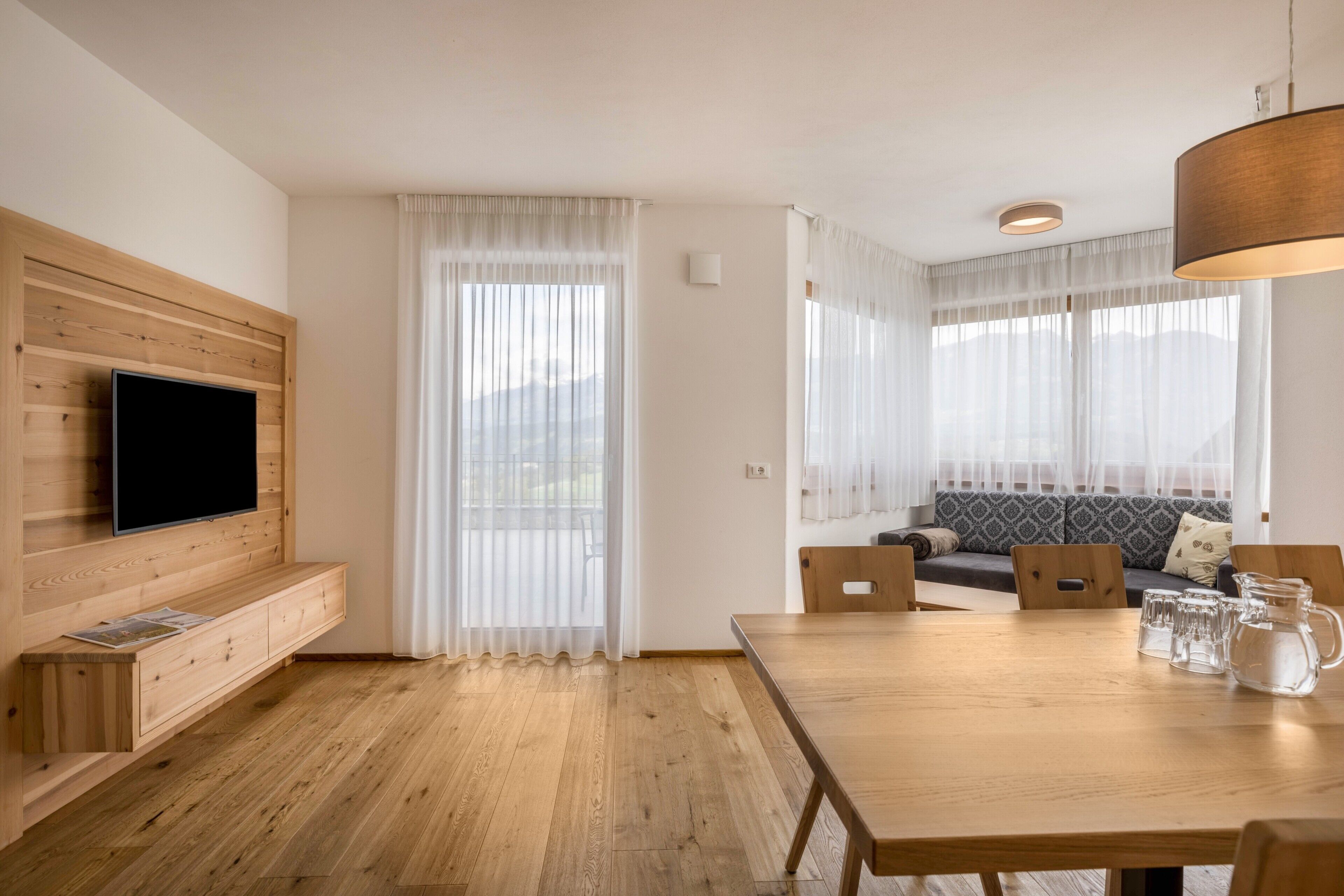 Ein modernes Wohnzimmer mit Flachbildfernseher, einer Holz-Unterhaltungseinheit, Esstisch und einer gemütlichen Sitzecke mit Sofa und Sesseln.