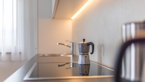Een moderne keuken met een roestvrijstalen koffiezetapparaat op een reflecterend aanrecht, een waterkoker en een kraan op de muur.