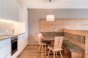 A modern kitchen with a built-in oven, a dining area with wooden benches, and a pendant light.