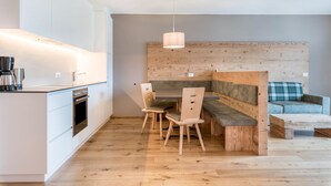Een moderne keuken met witte kasten, een inbouwoven en een eethoek met houten stoelen en een bank.