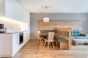 A modern kitchen with white cabinets, a built-in oven, and a dining area with wooden chairs and a bench.