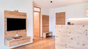 Een moderne woonkamer met een flatscreen televisie aan een houten wand, een houten bankje en een houten scheidingswand.