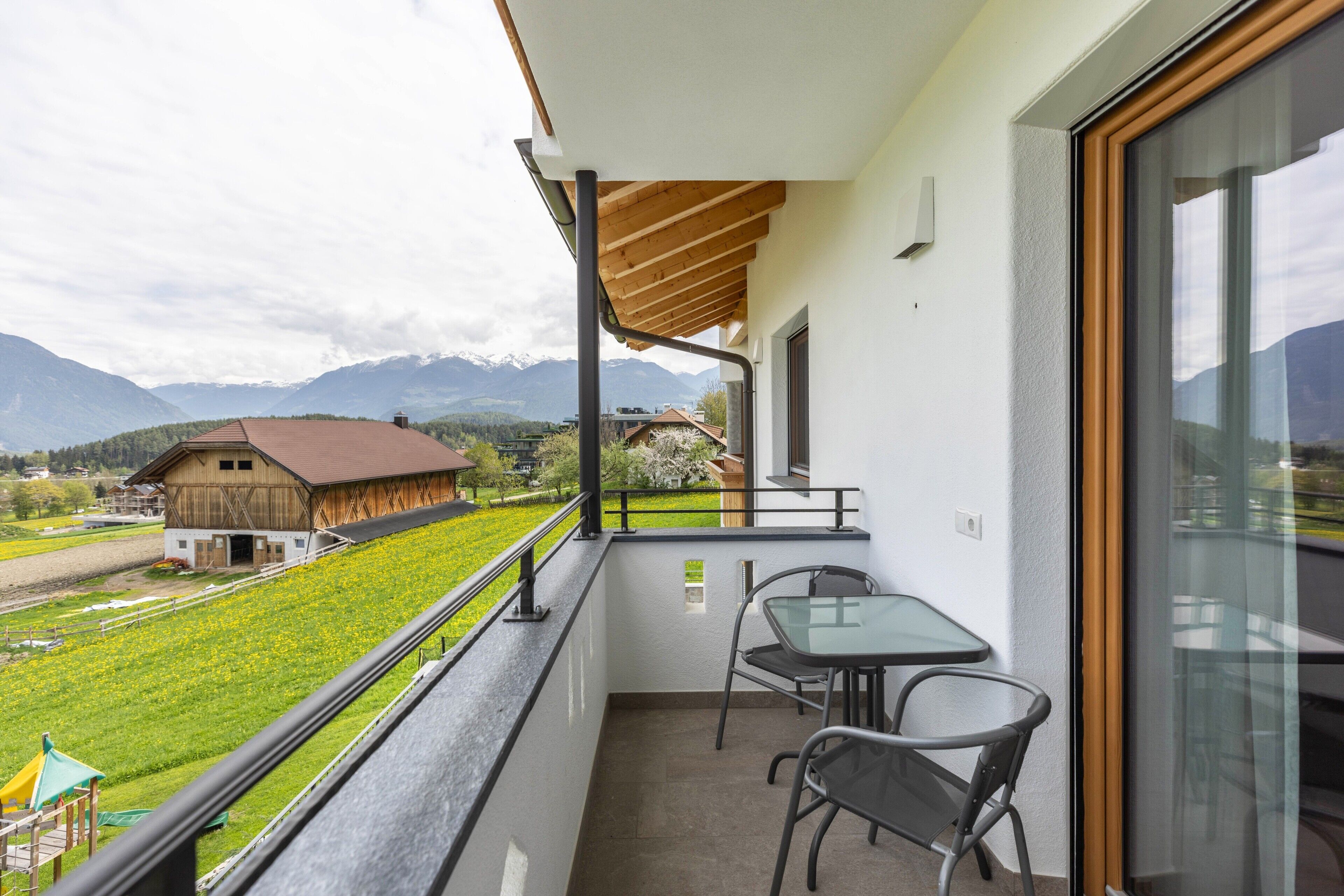 A balcony with a table and chairs, a view of a mountain, and a building with a red roof.