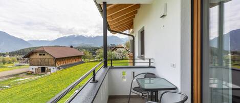 A balcony with a table and chairs, a view of a mountain, and a building with a red roof.