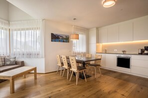 A modern kitchen with white cabinets, a dining table with chairs, a wooden bench, and a pendant light.