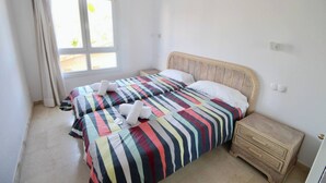 A bedroom with two beds, a window, a wooden nightstand, and a door. - El Amanecer 81 by homeprive (Denia)
