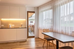 A modern kitchen with a wooden countertop, a kettle, and a sink. There is a dining area with a table and chairs.