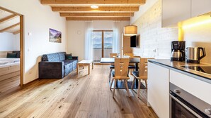 Una cocina moderna con vigas de madera, un comedor con mesa y sillas, un sofá y vistas a las montañas a través del ventanal.