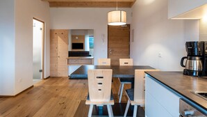 A modern kitchen with wooden flooring, a dining table with chairs, a coffee maker, and a hanging light fixture.