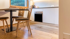 A modern kitchen with white cabinets, a built-in oven, and a dining area with a table and chairs. - Apartment "Stefansdorf Wohnung 9" with Mountain View, Wi-Fi, Garden, Balcony, and Barbecue (St. Lorenzen)