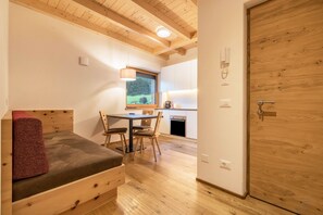 A compact room with a bed, a dining table, chairs, a small kitchen area, and a wooden door.