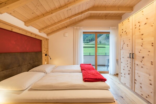 A bedroom with a wooden ceiling, a large window, and a view of a green landscape.