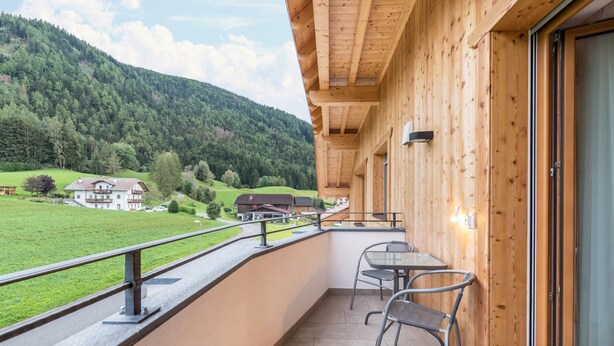 A balcony with a view of a green valley and a mountain, a wooden exterior wall, and a table with chairs. - Apartment "Stefansdorf Wohnung 9" with Mountain View, Wi-Fi, Garden, Balcony, and Barbecue (St. Lorenzen)