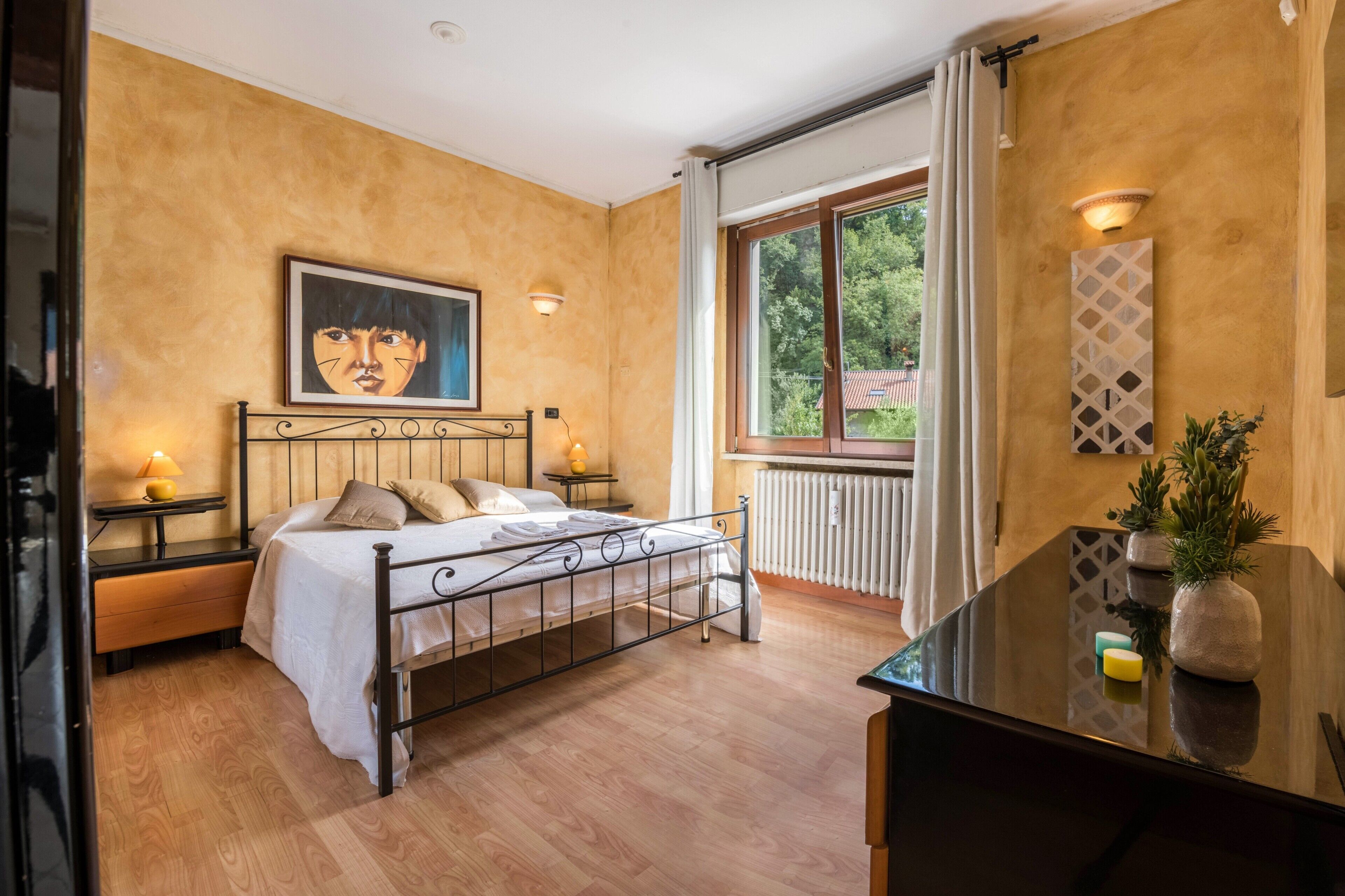 Een slaapkamer met een bed, nachtkastjes, een radiator en een wandlamp, plus een raam met gordijnen.