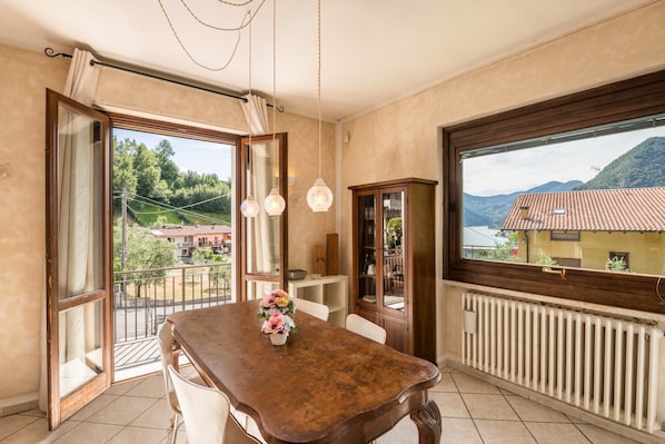 Una habitación con una mesa de madera, vistas a montañas, un radiador y una ventana con cortinas.