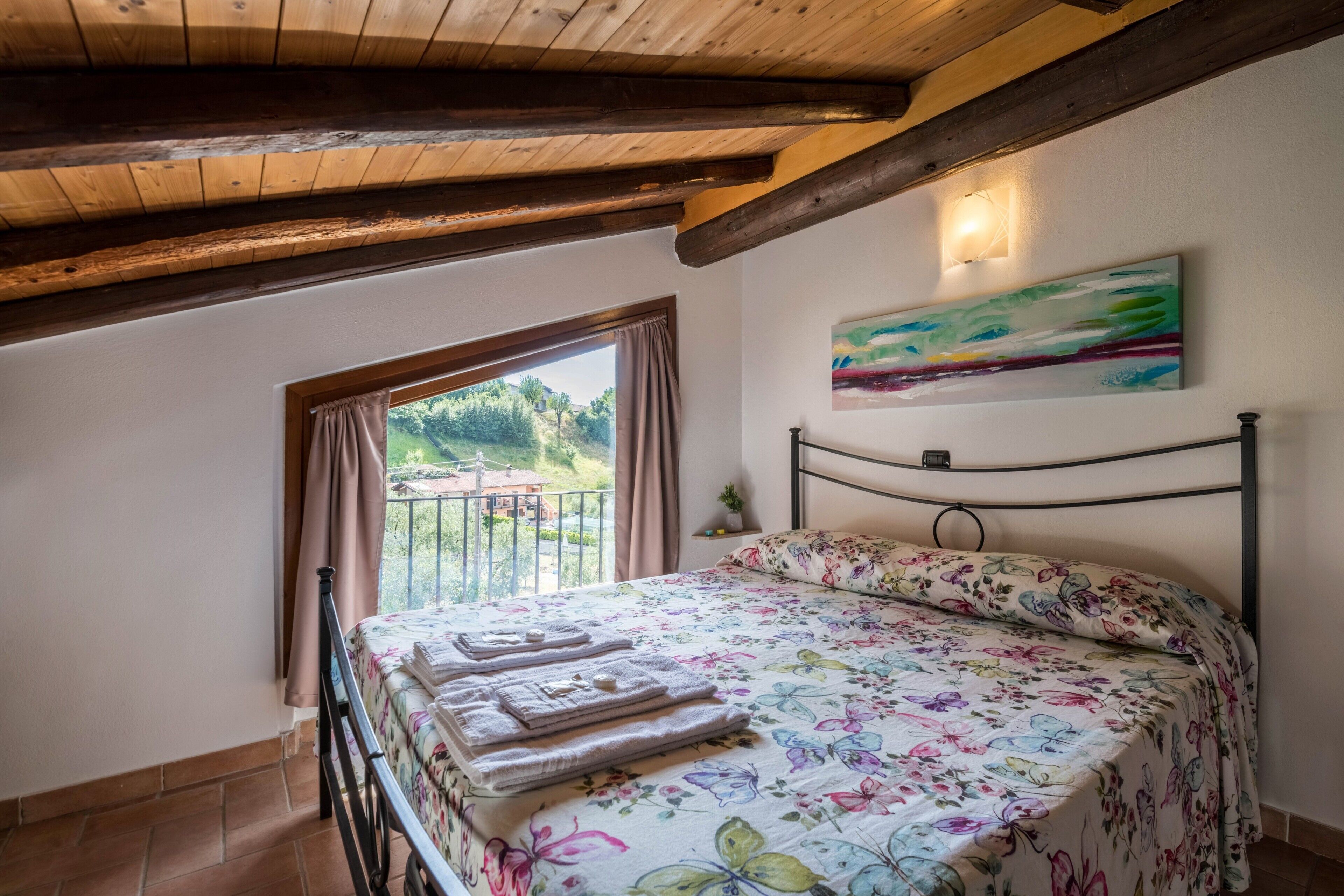 Un dormitorio con una cama, una ventana con cortinas, un cuadro en la pared y un techo de madera.