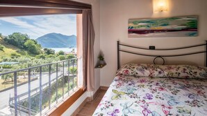 Ein Schlafzimmer mit Balkon, einem Bett mit floralem Bettbezug, einem Gemälde an der Wand und Blick auf Berge.
