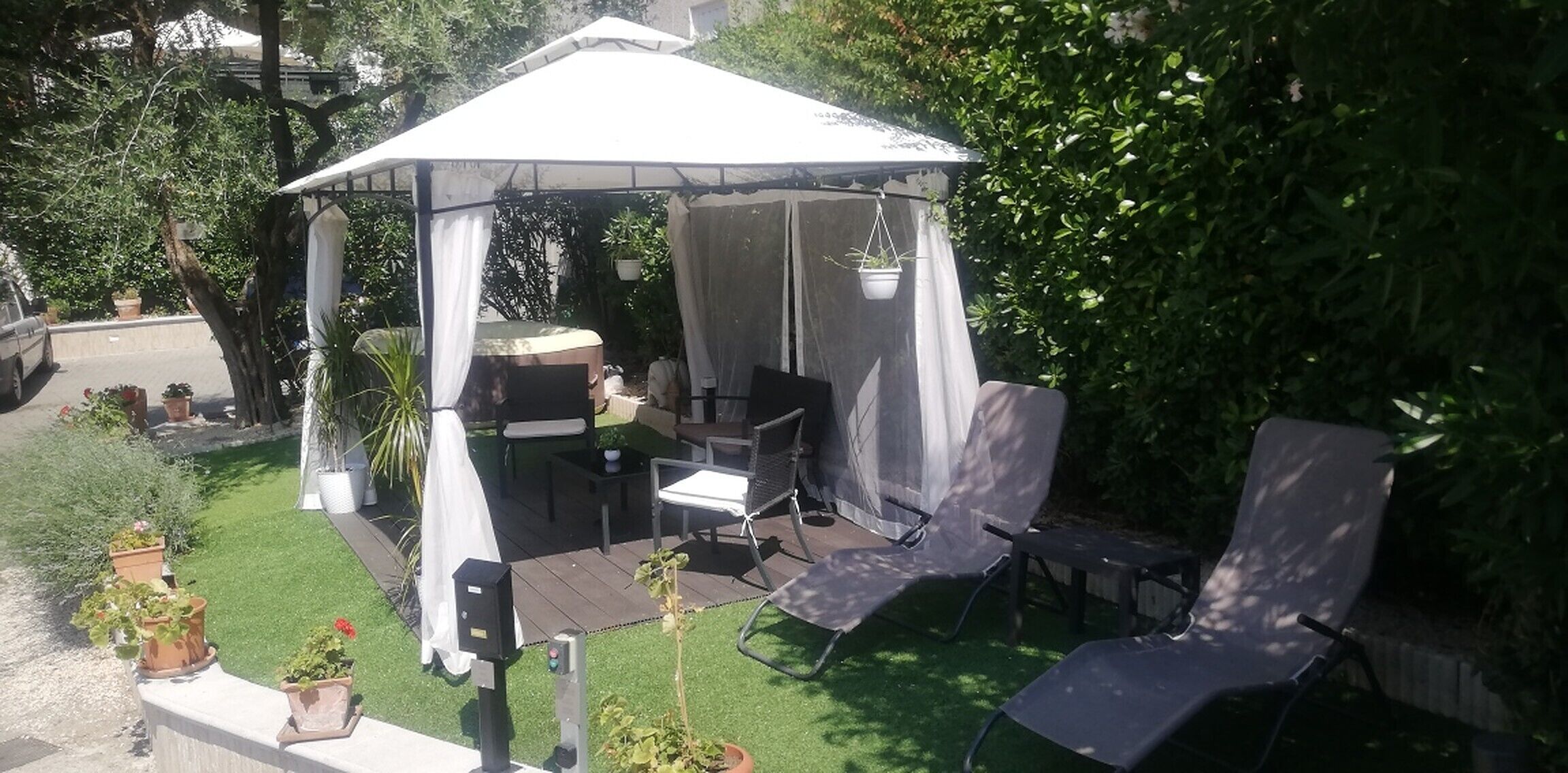 A gazebo with a table and chairs, surrounded by potted plants and a grassy area.