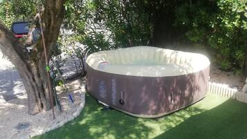 Un jacuzzi en un jardín con un árbol y una valla.