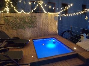 Area piscina con pavimento in legno, luci a tendina e parete in bambù.