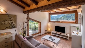 Ein Wohnzimmer mit einer Couch, einem Couchtisch, einem Fernseher und einem großen Fenster mit Blick auf die Berge.
