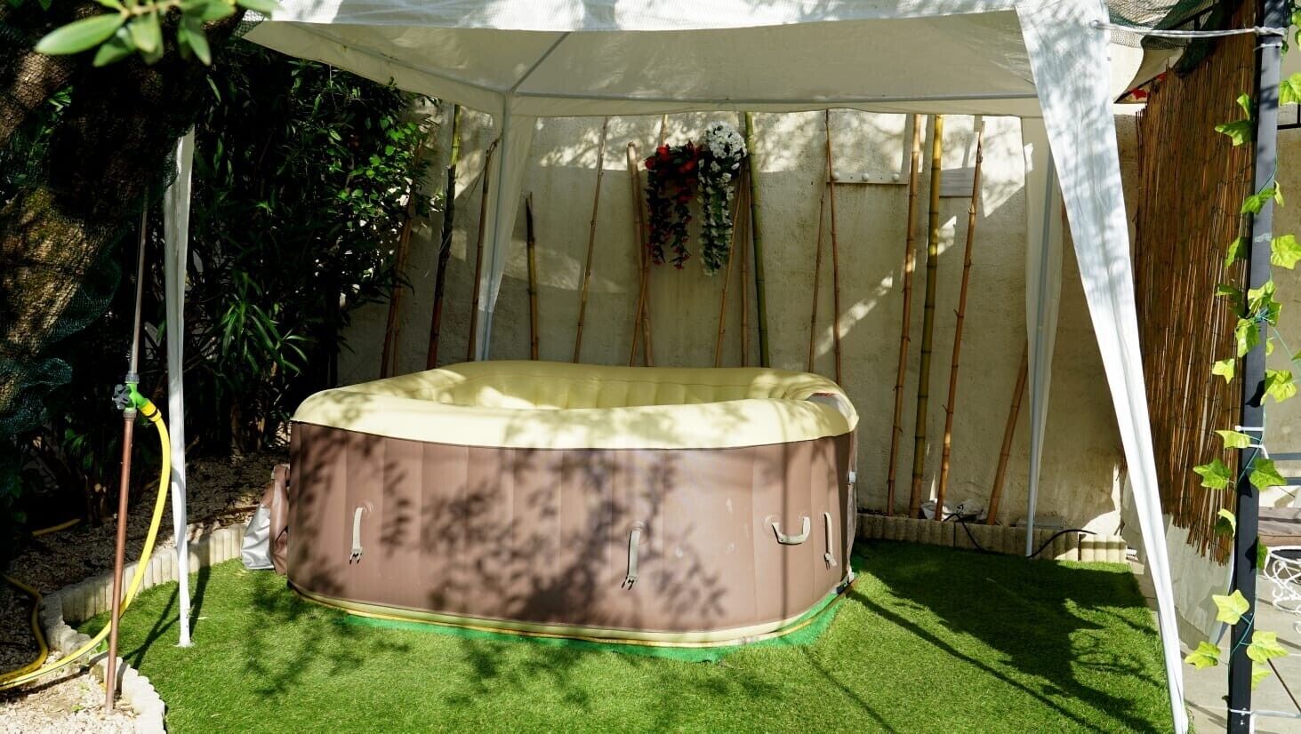 A hot tub under a canopy with bamboo poles and a hanging flower arrangement.