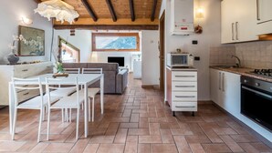 Eine moderne Küche mit weißen Schränken, ein Essbereich mit weißem Tisch und Stühlen und ein großes Fenster mit Blick auf eine gebirgige Landschaft.