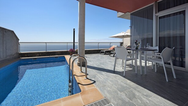 A swimming pool with a view of the sea, a covered outdoor area with a table and chairs, and a large window. - Villa View Grand with Sea View, Pool & Wi-Fi (Santa Ursula)