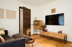En moderne stue med sofa, sofabord med vase, et træskab og et fladskærms-tv monteret på væggen.