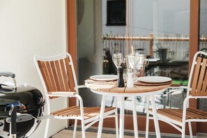 Una mesa redonda de madera con sillas blancas, una parrilla y una botella de champán.