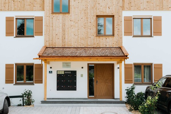 Ein Gebäude mit Holzfassade, mehreren Fenstern mit Fensterläden, einer Tür und einem kleinen Garten mit Pflanzen.