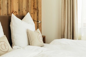 Una cama bien hecha con ropa de cama blanca y varias almohadas, un cabecero de madera y una mesita de noche con una lámpara.