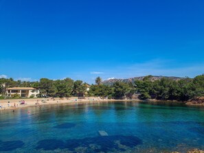 A beach with clear water, a sandy shore, and buildings in the background.